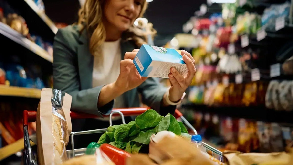 Woman reading a product label while grocery shopping, illustrating how to evaluate a supplement or food label accurately while standing in the aisle for MaxiMeal blog
