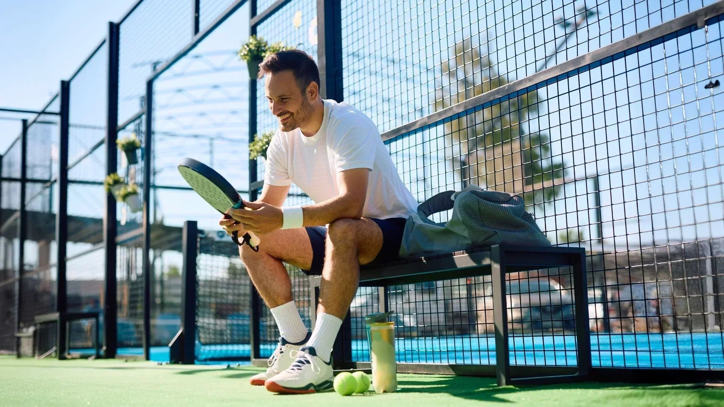 Adult man drinking from a bottle while resting on an outdoor padel court, illustrating recovery and nutrition needs for active adults training over 30 for MaxiMeal Blog