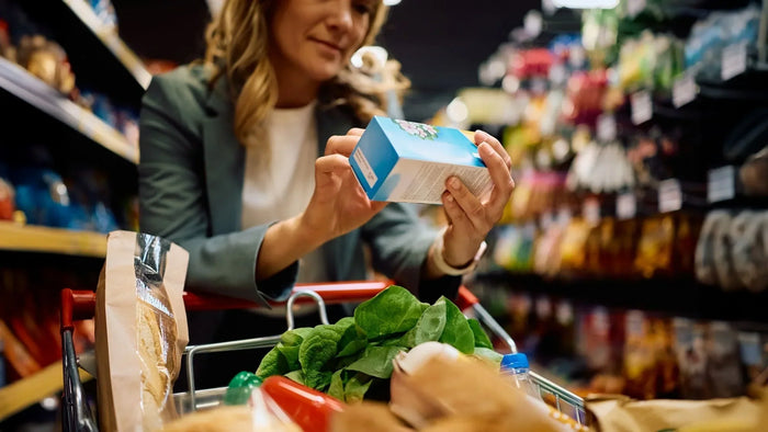Woman reading a product label while grocery shopping, illustrating how to evaluate a supplement or food label accurately while standing in the aisle for MaxiMeal blog
