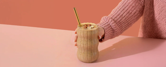 MaxiMeal Double Thick Shake in a glass with a straw on a pink background