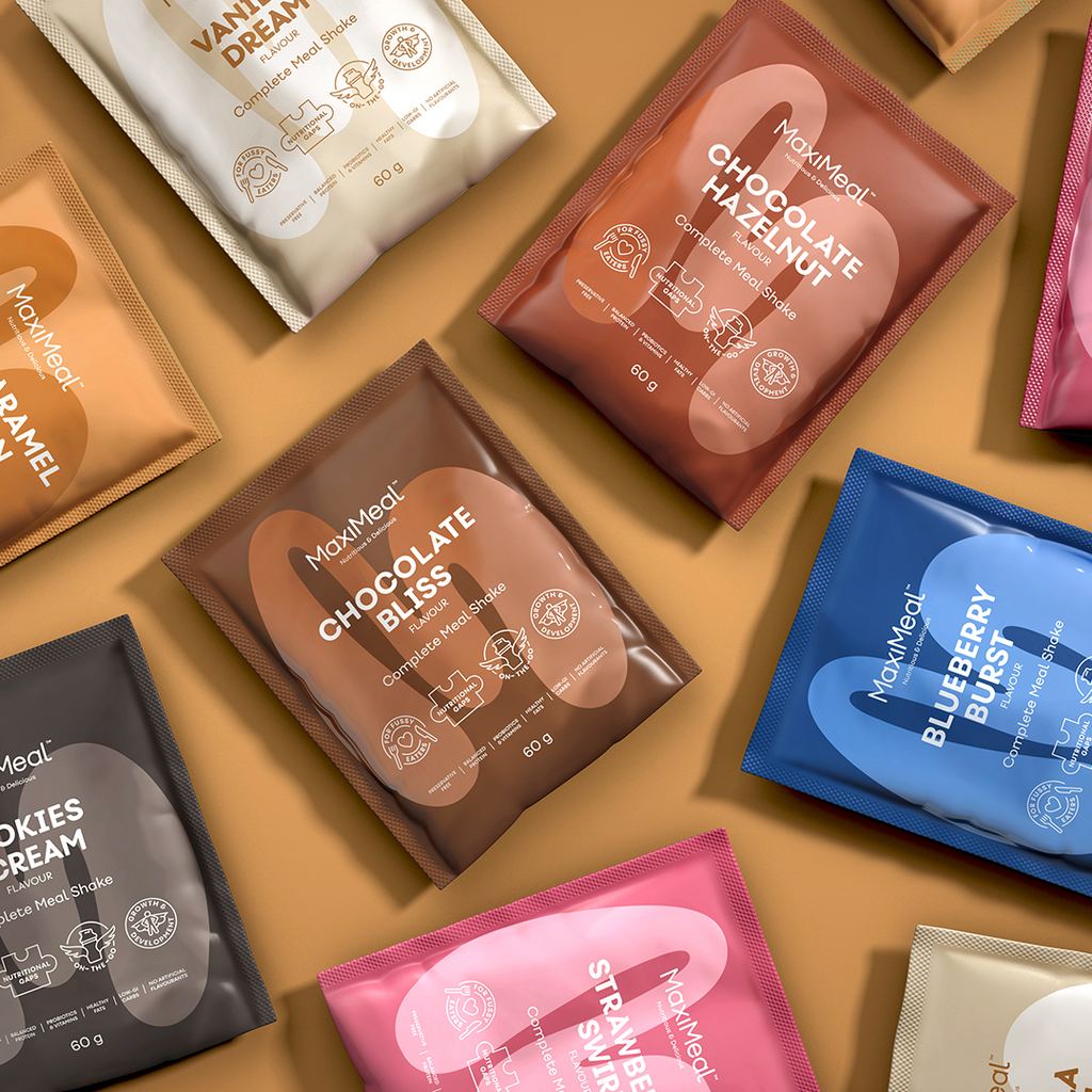 MaxiMeal complete meal shake sachet range laid flat showing Chocolate Bliss, Chocolate Hazelnut, Blueberry Burst, Strawberry Swirl, Vanilla Dream, Cookies and Cream, and Caramel flavours, non-GMO, maltodextrin free, no artificial sweeteners.